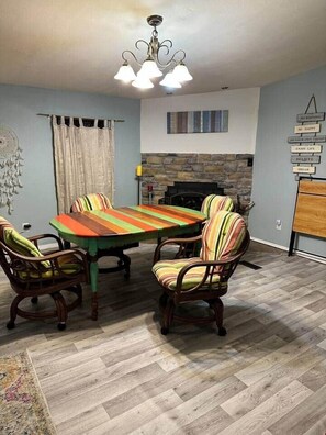 A dining area with a large table, four striped chairs, a chandelier, a stone fireplace, and a wall with motivational signs.