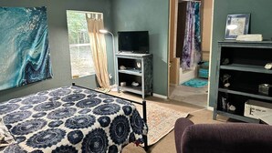 A bedroom with a bed, a TV, a bookshelf, and a door leading to another room.