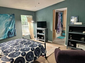 A bedroom with a bed, a TV, a bookshelf, and a door leading to another room.