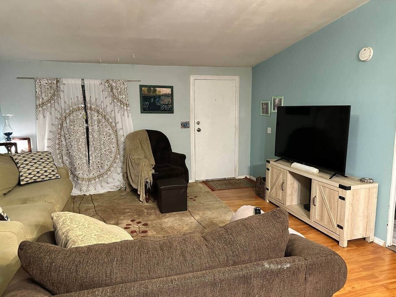 A living room with a sofa, a chair, a television on a wooden cabinet, and a door.
