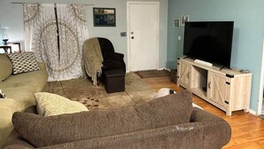 A living room with a sofa, a chair, a television on a wooden cabinet, and a door.