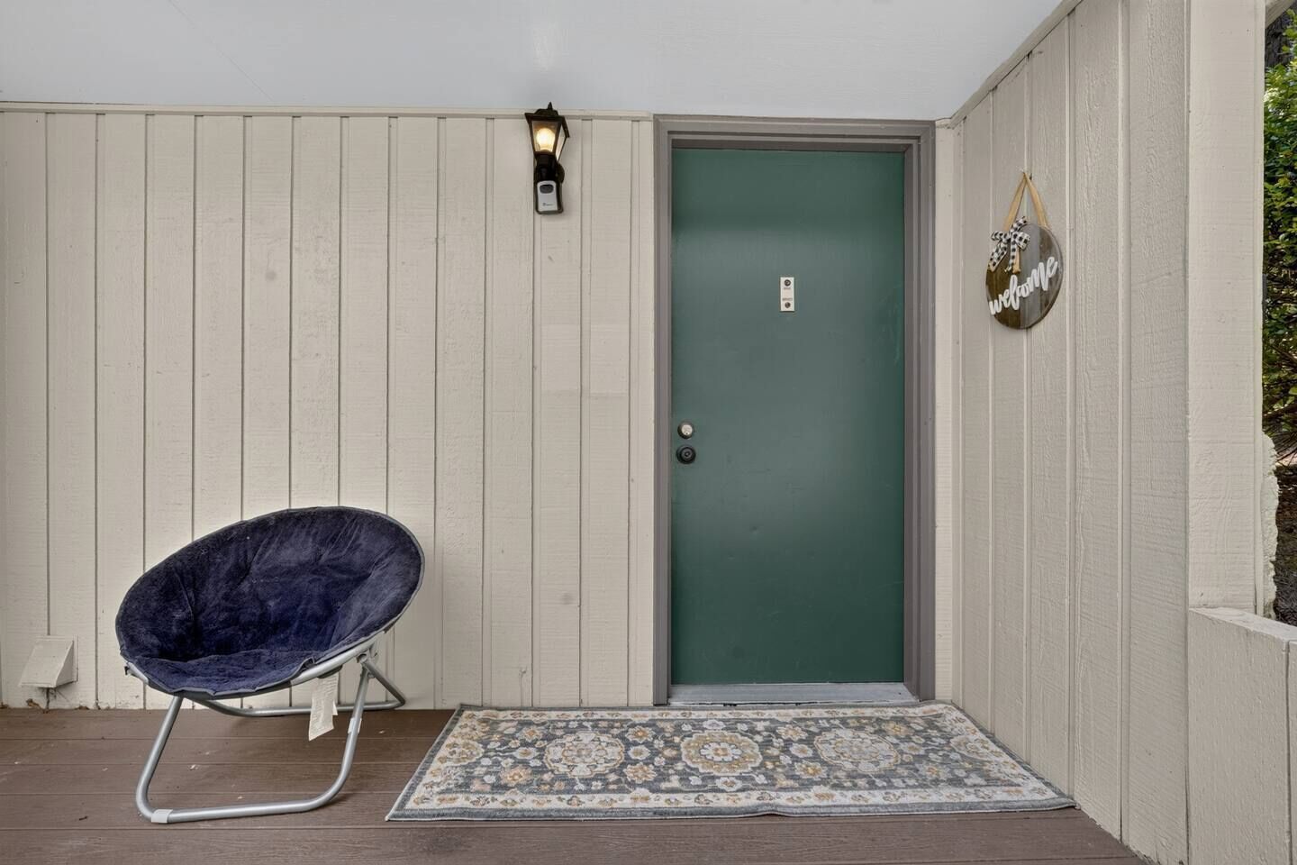 A door with a green door frame, a welcome sign, a chair, and a patterned rug.