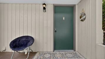 A door with a green door frame, a welcome sign, a chair, and a patterned rug.
