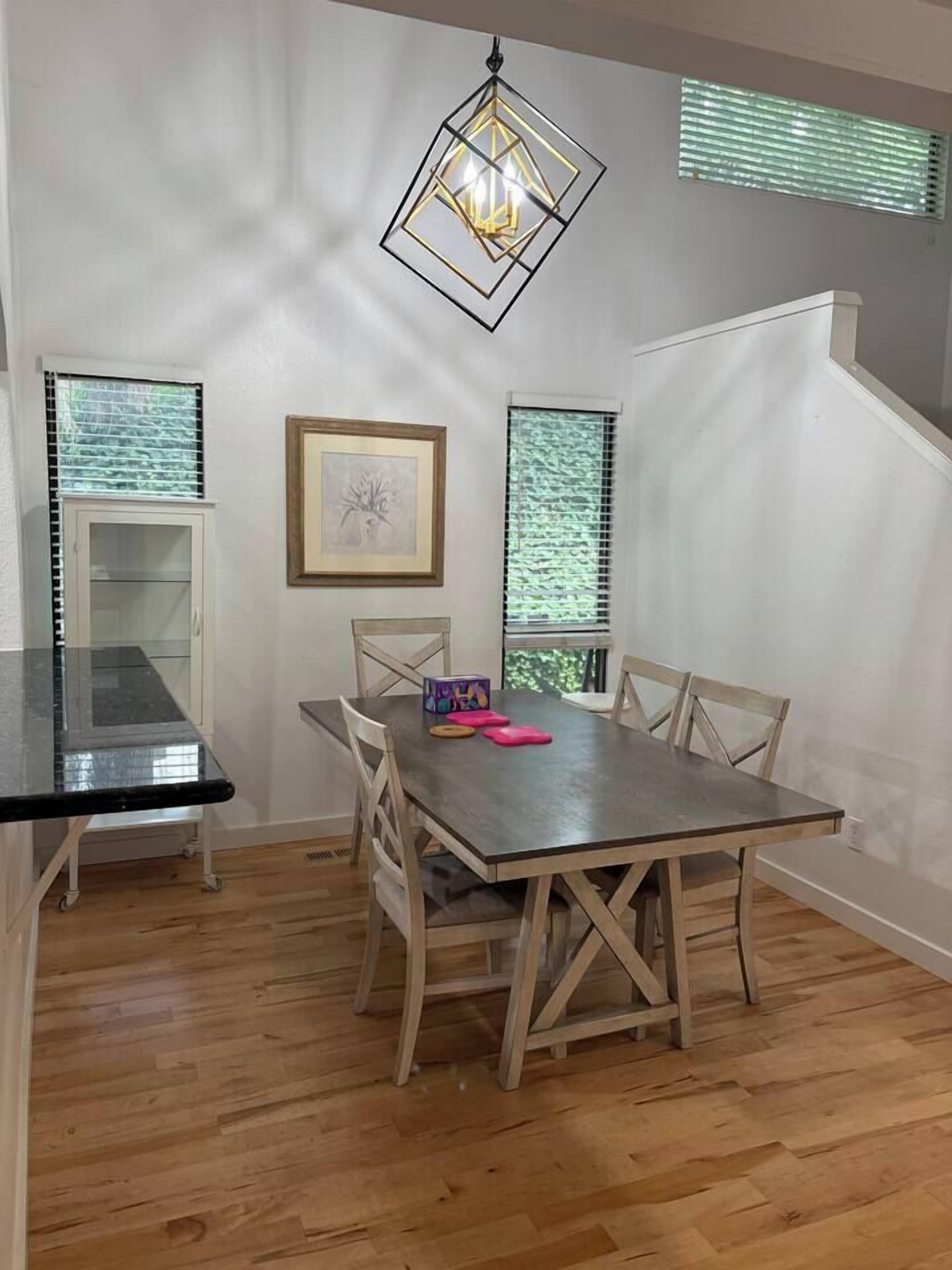 A dining area with a wooden table and chairs, a chandelier, and a window with blinds.