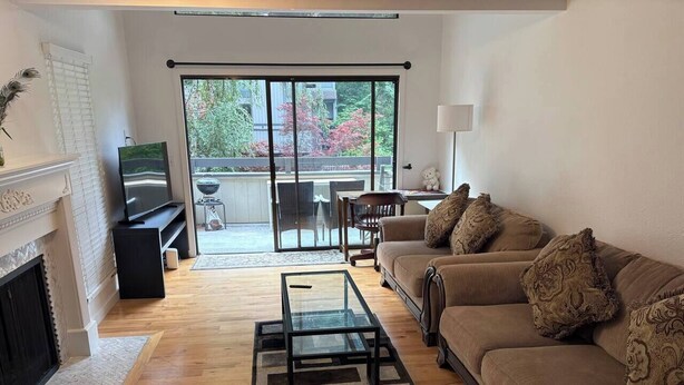A living room with a sofa, a glass coffee table, a fireplace, and a sliding glass door leading to an outdoor area. - Stylish 2BR Near Bellevue & Kirkland w/ Pool+AC (Bellevue)