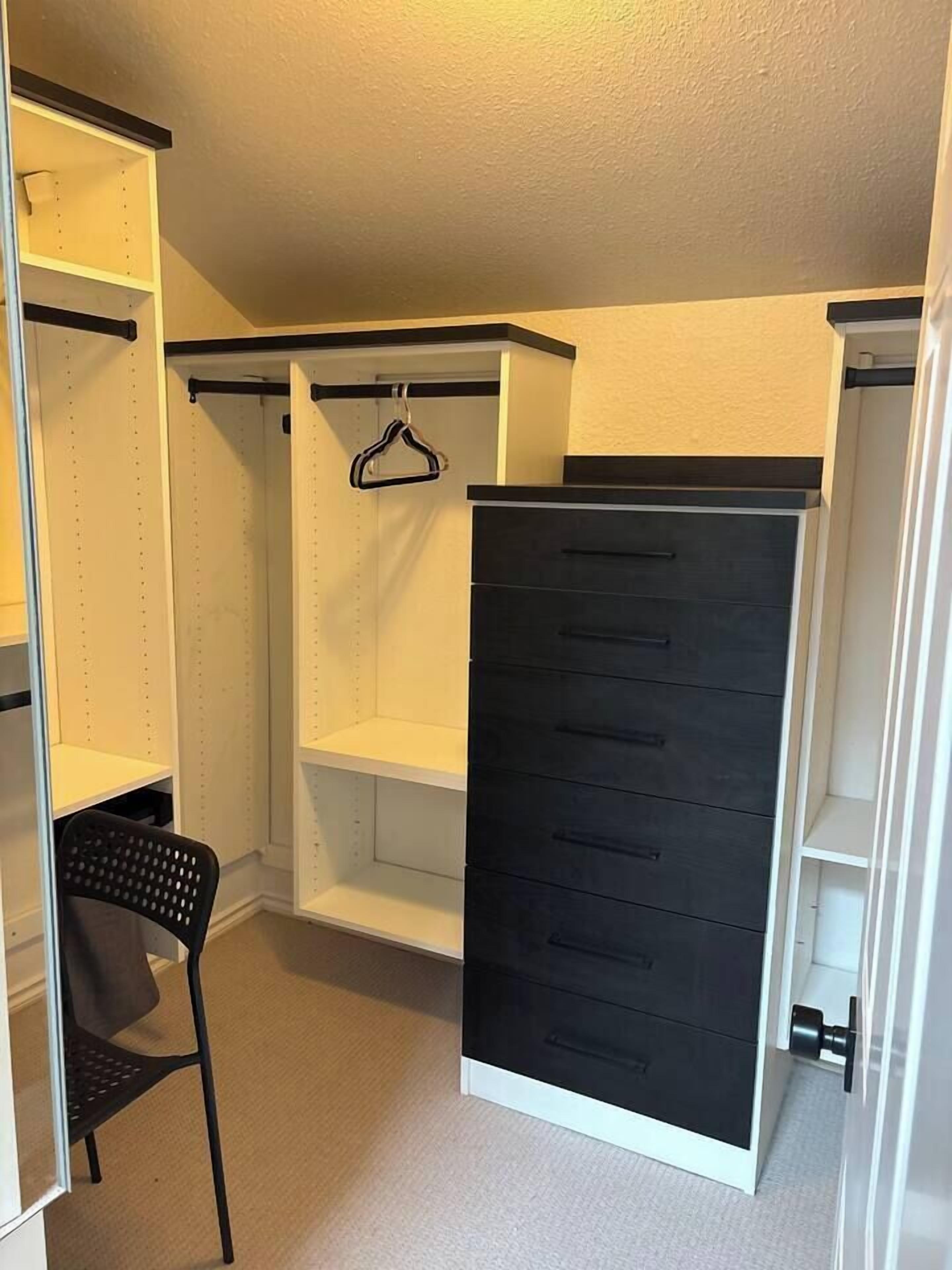 A walk-in closet with open shelving, a black hanging rod, and a black storage unit with multiple drawers.