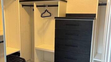 A walk-in closet with open shelving, a black hanging rod, and a black storage unit with multiple drawers.