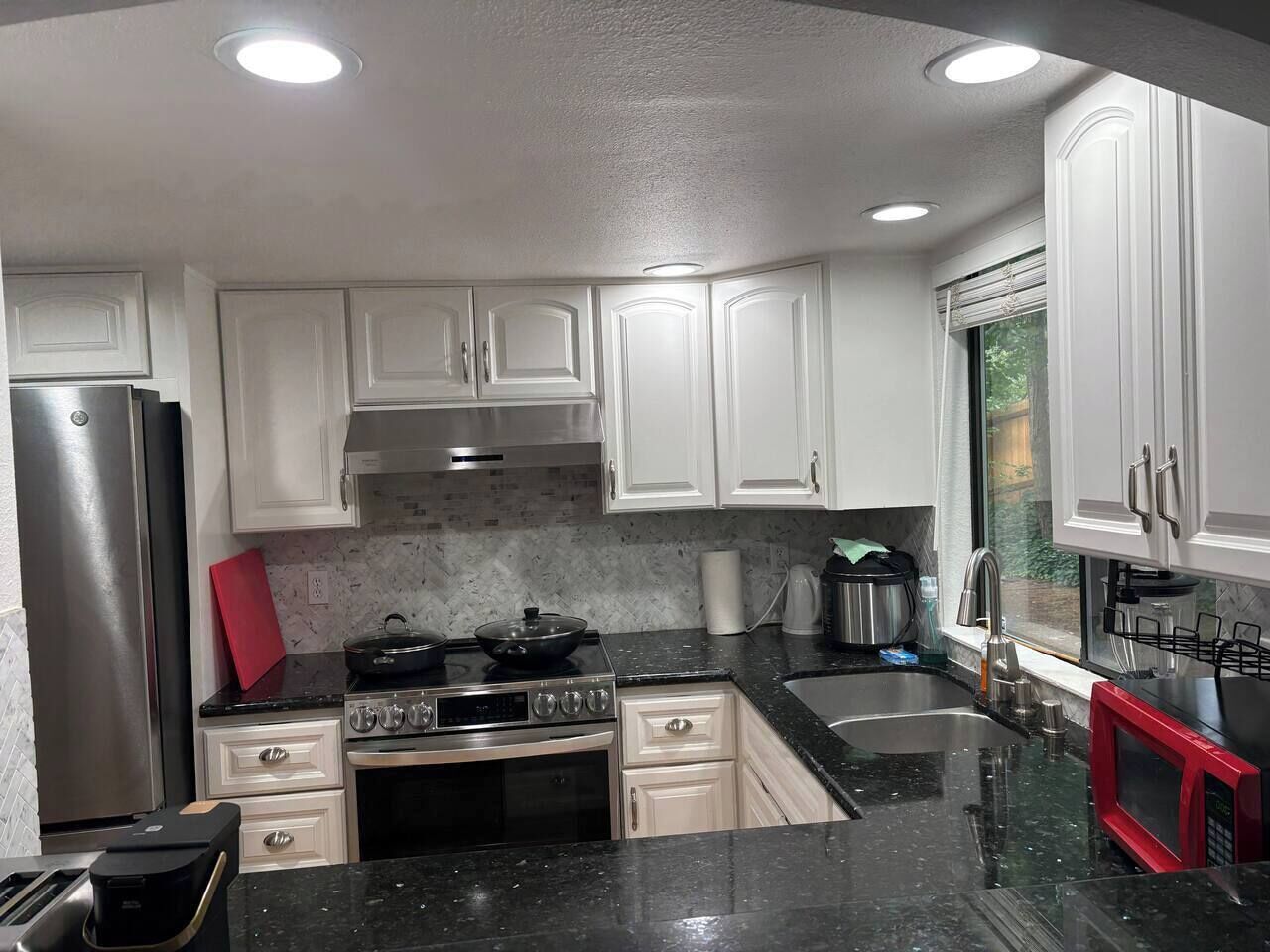 A kitchen with white cabinets, a stainless steel refrigerator, a black stove, and a red microwave.