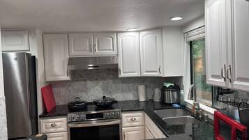 A kitchen with white cabinets, a stainless steel refrigerator, a black stove, and a red microwave.