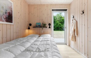 Ein Schlafzimmer mit einem Bett, einer Tür, die nach draußen führt, einem Wandregal mit einer Pflanze und einem Bild an der Wand.