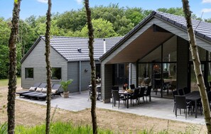 Ein modernes Haus mit einer Terrassenfläche, ausgestattet mit einem Esstisch und Stühlen, umgeben von Bäumen.