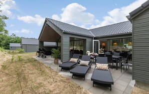 Un'area salotto esterna riparata, con poltrone reclinabili e tavoli, un barbecue e un'uscita con porta in vetro verso un patio.