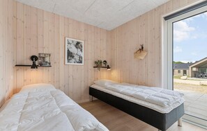 A room with two beds, wooden walls, a framed picture, a lamp, and a basket. - Awesome home in Glesborg with sauna (Glesborg)