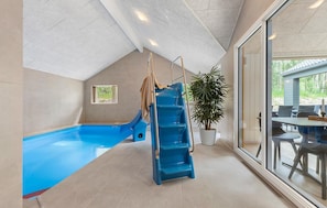 A pool area with a blue slide and a small pool, a potted plant, and a view of the outdoors through a glass door. - Awesome home in Glesborg with sauna (Glesborg)