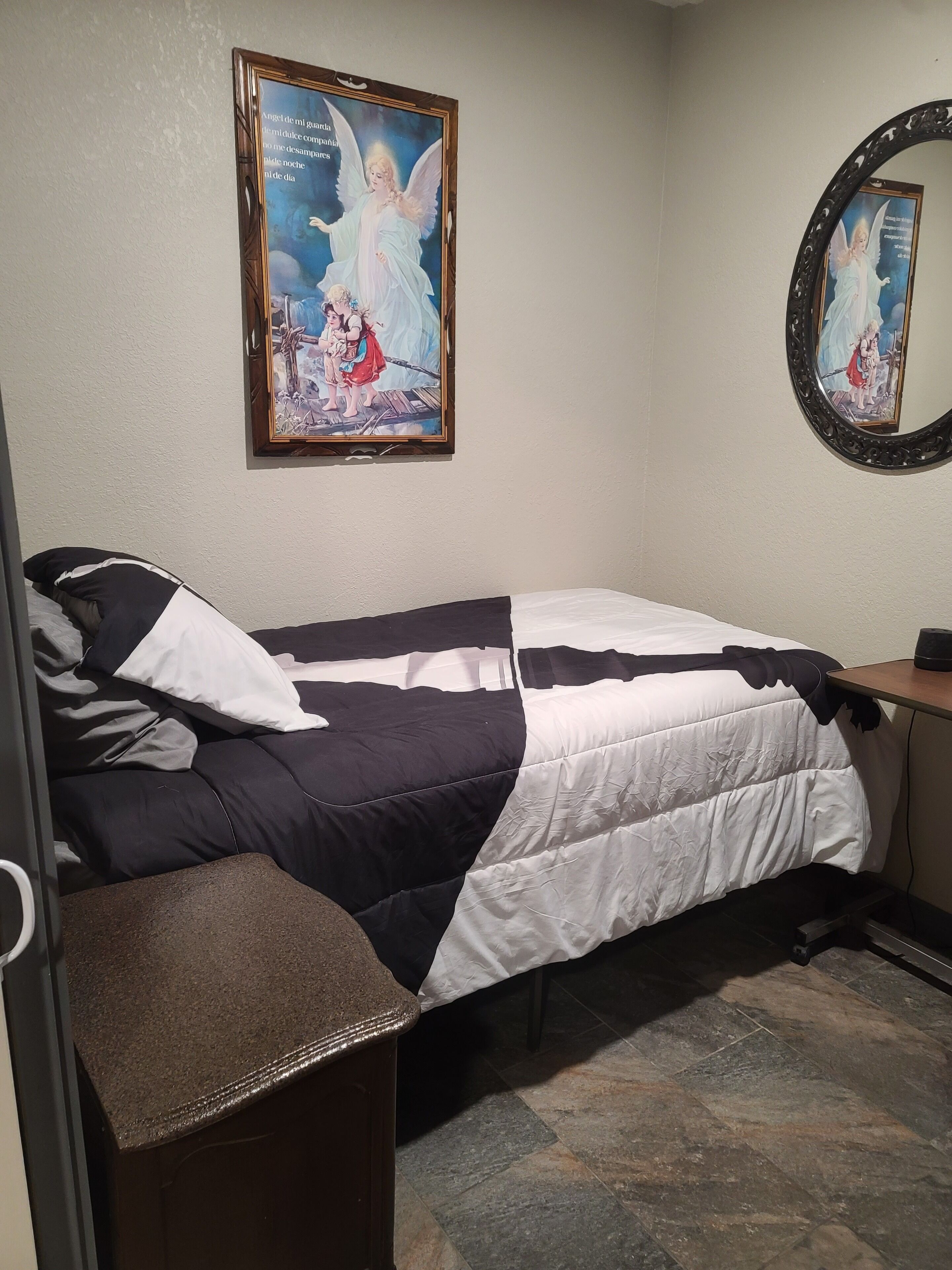 Un dormitorio con cama, mesita de noche, espejo y un cuadro en la pared.