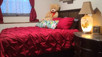 Un dormitorio con una cama, un osito de peluche, una lámpara y un cuadro en la pared.