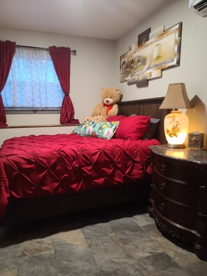 Une chambre à coucher avec un lit, un ours en peluche, une lampe et un tableau accroché au mur.