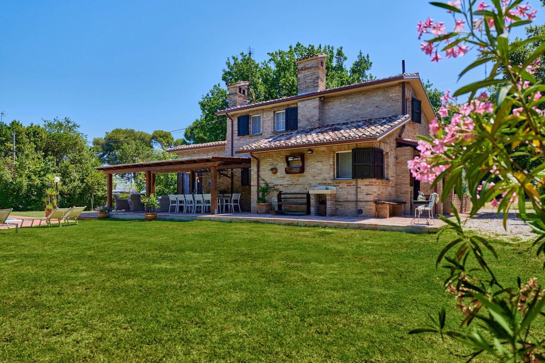 Ein zweigeschossiges Steinhaus mit überdachter Terrasse, Sitzgelegenheiten im Freien und einem gepflegten Rasen.
