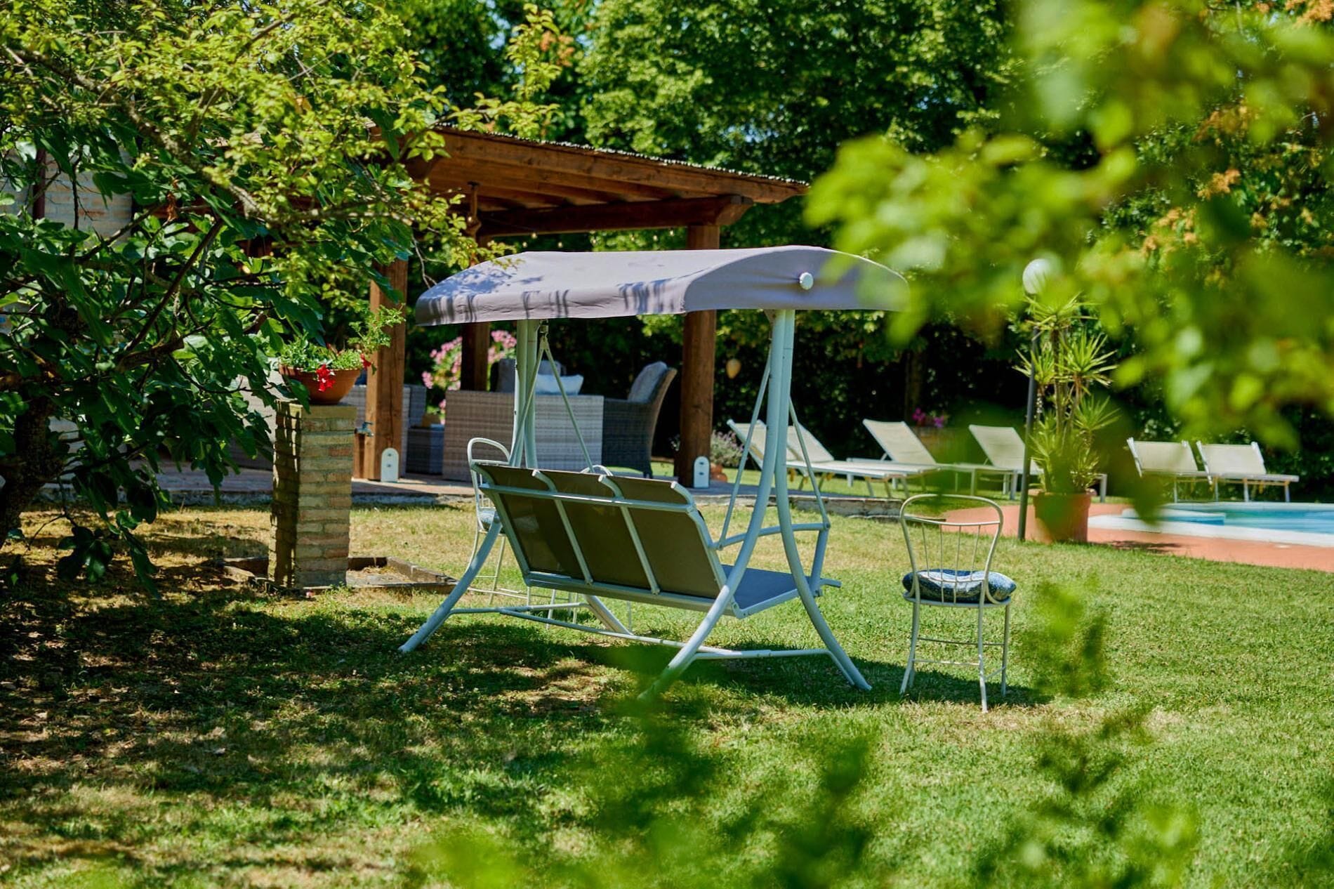 Ein überdachter Außenbereich mit Schaukelstuhl, einer kleinen Überdachung und einem Pool im Hintergrund.