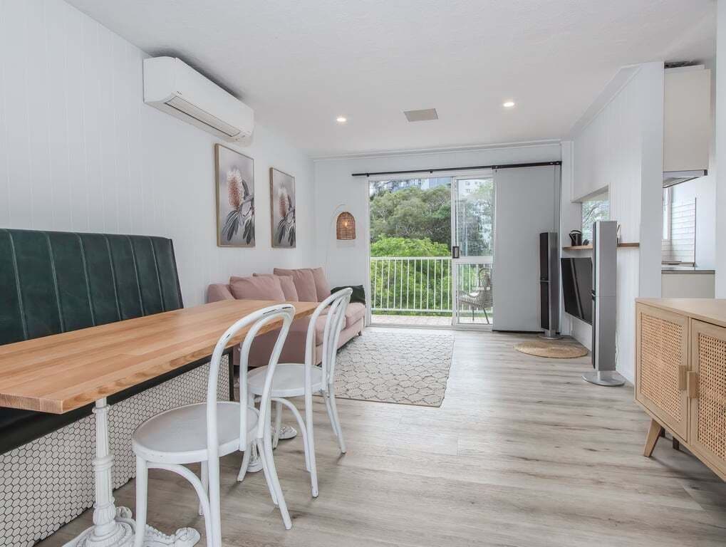 Uma cozinha moderna com mesa de madeira, cadeiras brancas e um banco estofado verde.