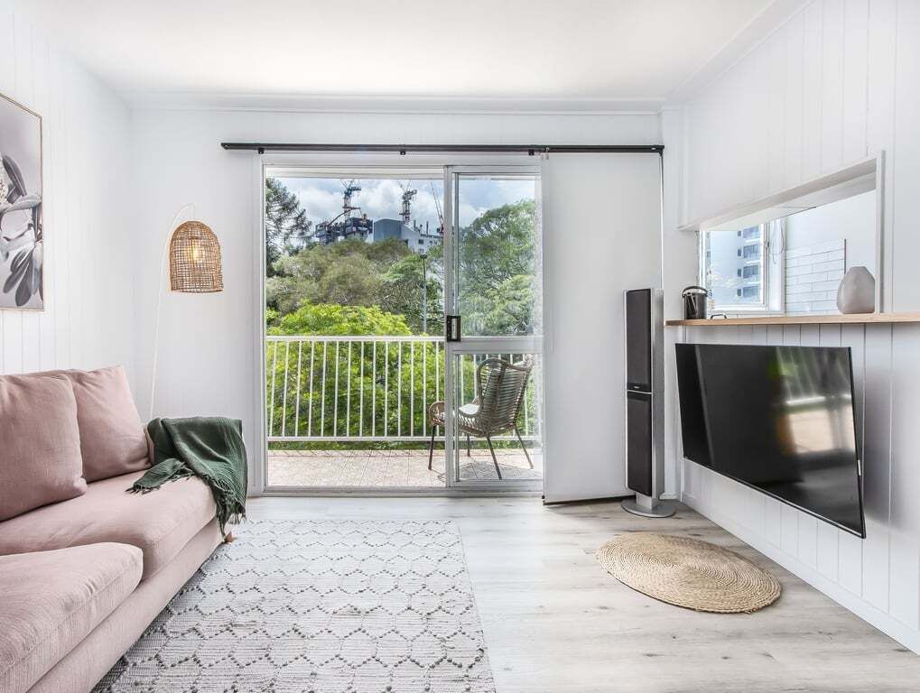 Ein modernes Wohnzimmer mit einer Couch, einem Fernseher und einer Schiebetür, die auf einen Balkon führt.