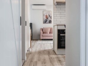 A hallway leading to a living area with a pink sofa, a framed picture on the wall, and a modern kitchen visible through an open door. - The Local Burleigh Heads (Gold Coast)