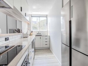 A modern kitchen with stainless steel appliances, white cabinetry, and a window providing natural light. - The Local Burleigh Heads (Gold Coast)