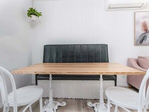 A dining area with a wooden table, white chairs, a cushioned bench, and a hexagonal patterned rug. - The Local Burleigh Heads (Gold Coast)