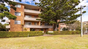 A multi-story residential building with a balcony on the ground floor, surrounded by well-maintained hedges. - The Pines Coastal Retreat Walk to Beach, BBQ, Sleeps 6 (Tuncurry)