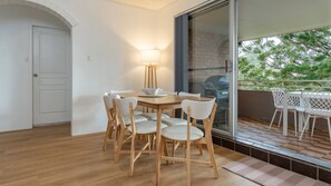 A dining area with a wooden table and chairs, a lamp, and a view of a balcony with outdoor furniture. - The Pines Coastal Retreat Walk to Beach, BBQ, Sleeps 6 (Tuncurry)