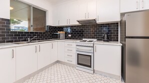 A modern kitchen with white cabinets, a stainless steel refrigerator, and a black tiled backsplash. - The Pines Coastal Retreat Walk to Beach, BBQ, Sleeps 6 (Tuncurry)