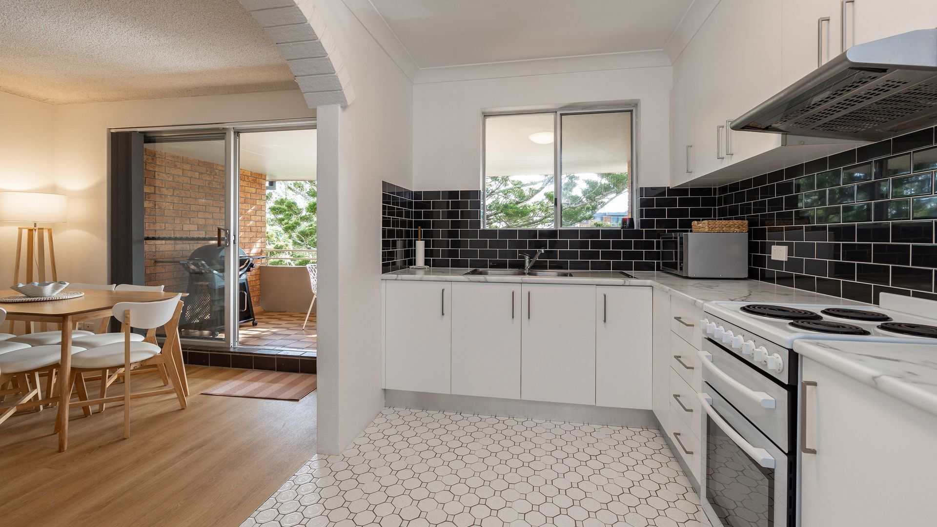 A modern kitchen with white cabinets, black backsplash, and a hexagonal patterned floor.