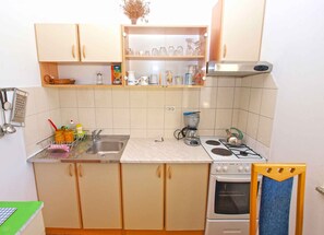 Une cuisine compacte équipée d’un évier, d’une cuisinière et d’un four, avec des meubles en bois et un dosseret carrelé.