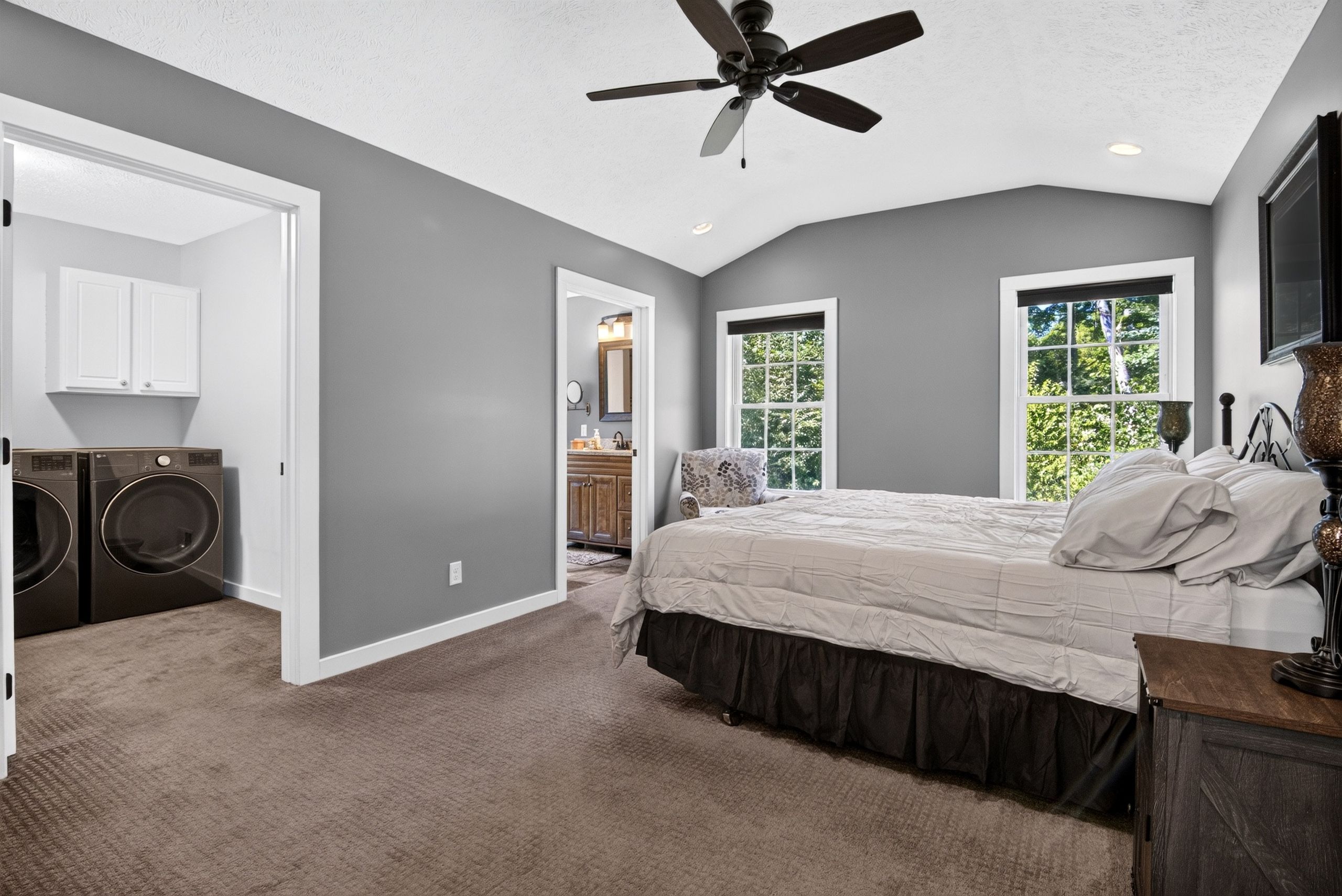 A bedroom with a bed, a ceiling fan, a window, and a door leading to a laundry area.