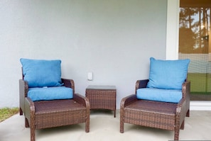 Two wicker chairs with blue cushions and a small wicker table between them, placed on a concrete patio. - Family Paradise Palm Coast Fire Pit Playground (Palm Coast)