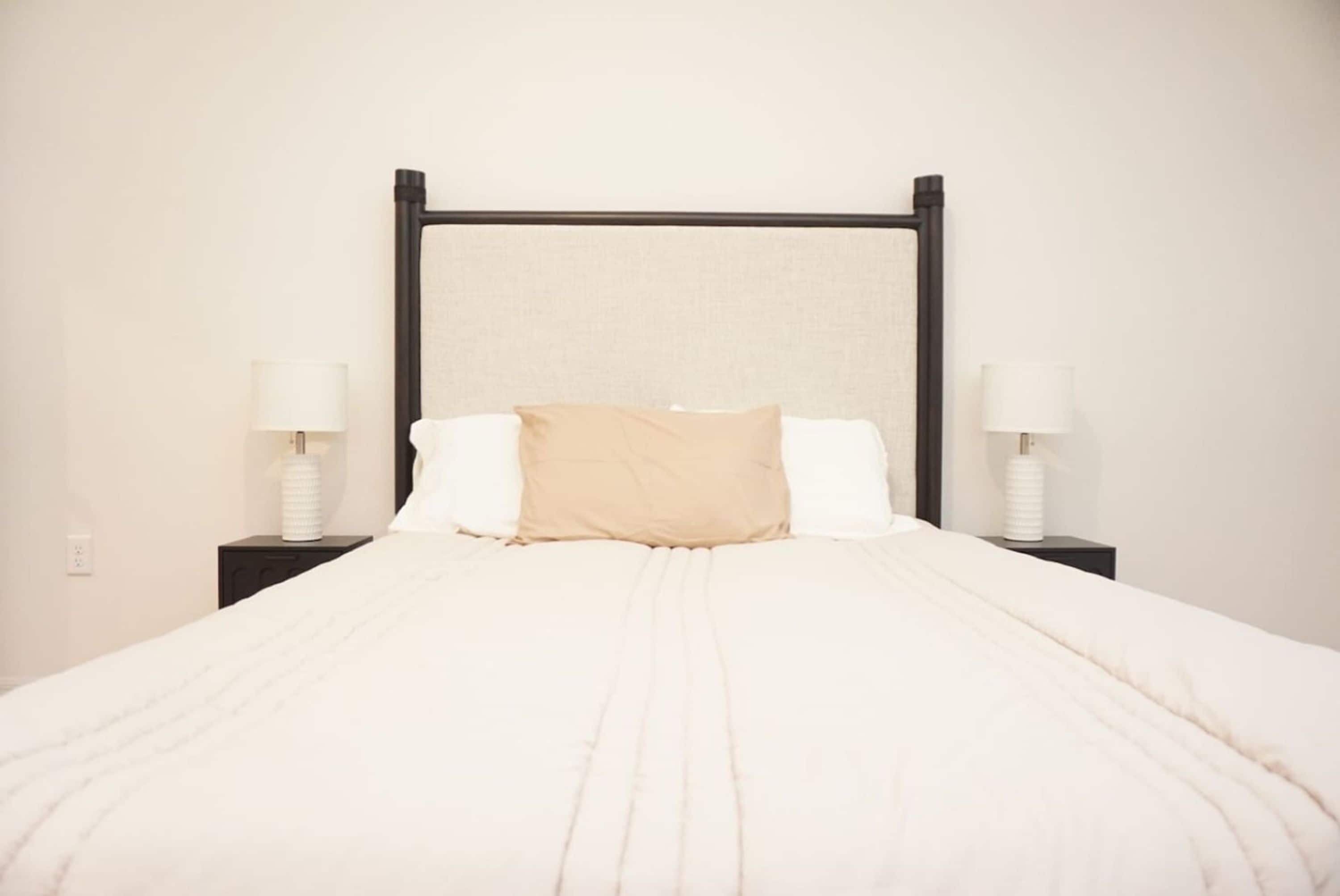A bed with a white bedspread and two pillows, flanked by nightstands with lamps.