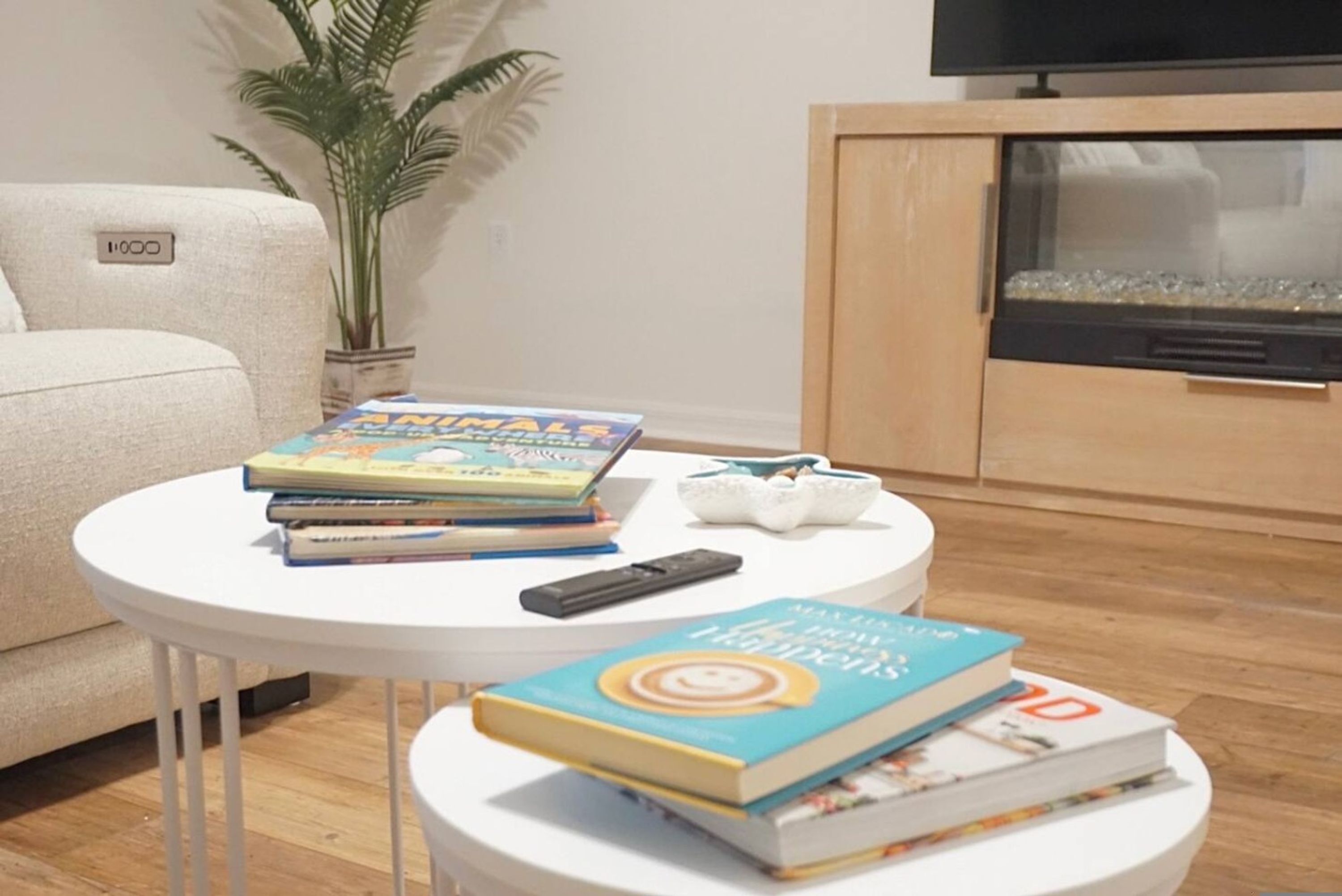 Ein Wohnzimmer mit einer Couch, einem Couchtisch mit Büchern, einer Fernbedienung und einem Fernseher auf einem Standfuß.
