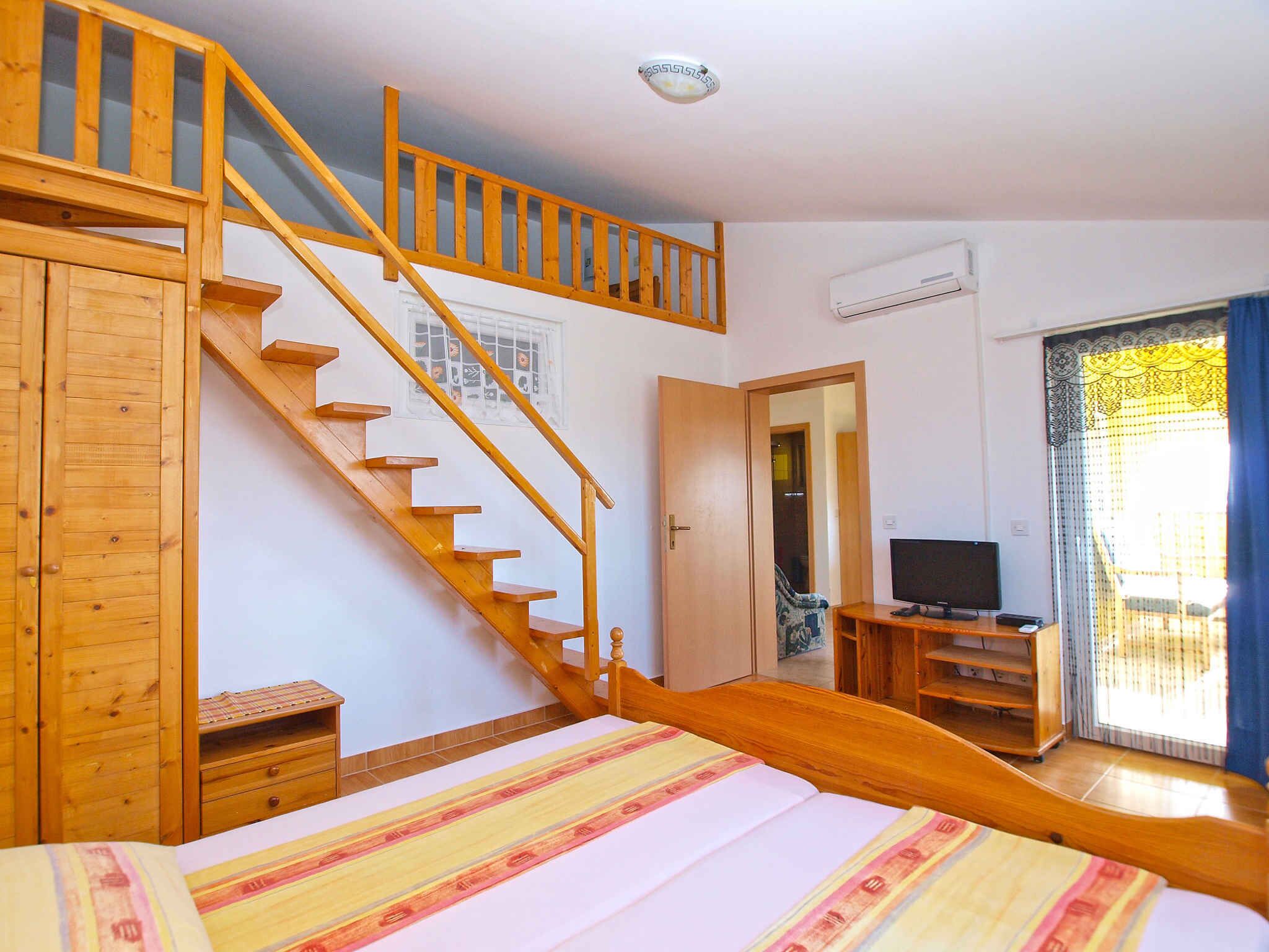 A bedroom with a wooden staircase, a bed with a striped bedspread, a television, and a window with curtains.