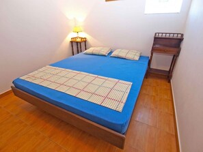 A single bed with a blue mattress and a patterned bedspread, a bedside table with a lamp, and a small wooden nightstand. - Holiday apartment with air conditioning (Valbandon)