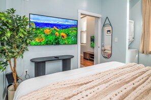 Une chambre à coucher avec un lit, un téléviseur fixé au mur, une plante et un miroir.