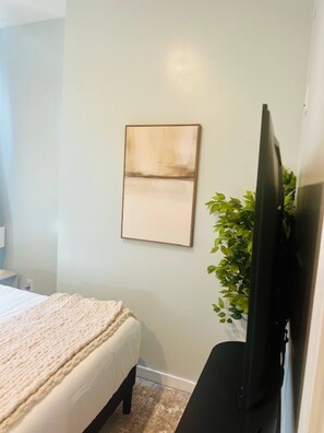 Een slaapkamer met een bed, een aan de muur bevestigde televisie en een plant.