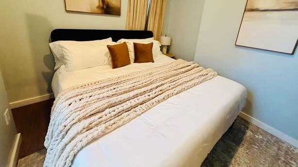 Cama bem arrumada com edredom branco e duas almofadas marrons, luminária de cabeceira e duas obras de arte emolduradas nas paredes.