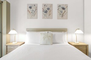 A hotel room with a bed, two bedside tables, a headboard, and three floral wall art pieces. - Saltwater Palms - Resort Living near Four Mile Beach (Port Douglas)