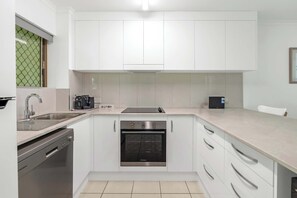 A modern kitchen with white cabinetry, stainless steel appliances, and a built-in oven. - Saltwater Palms - Resort Living near Four Mile Beach (Port Douglas)