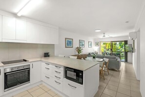 A modern kitchen with white cabinetry, a built-in oven, and a central island with a microwave. - Saltwater Palms - Resort Living near Four Mile Beach (Port Douglas)