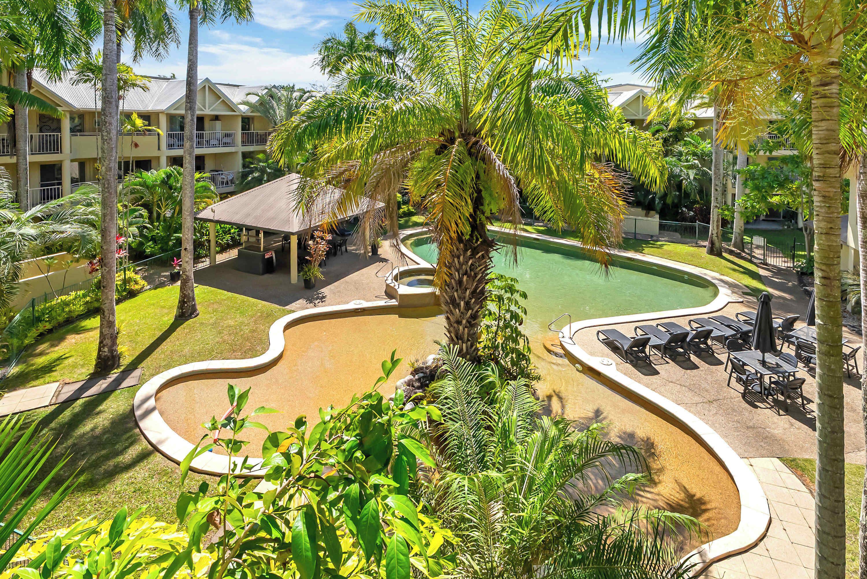A resort with a swimming pool, lounge chairs, and a covered seating area surrounded by palm trees.