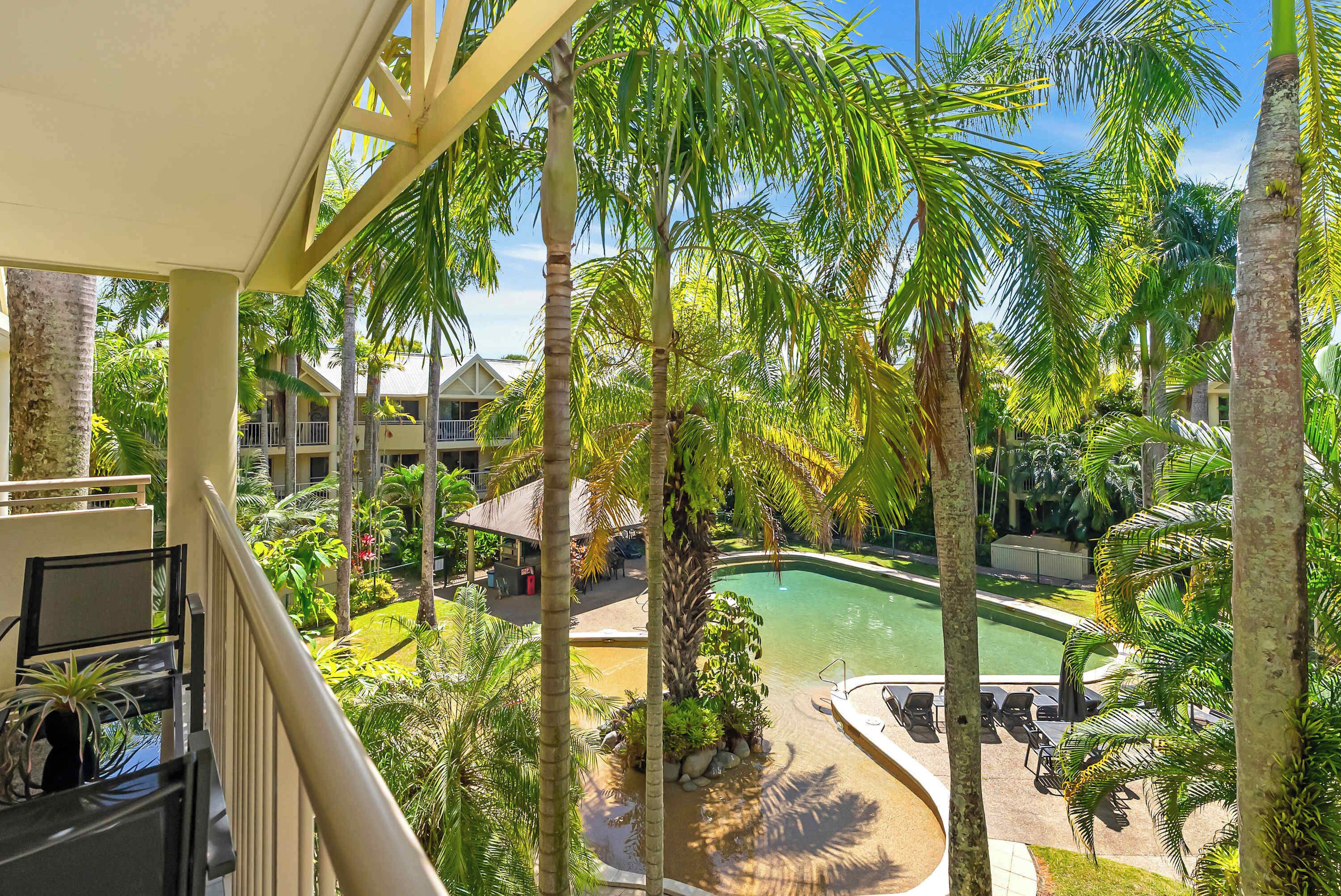 A pool surrounded by palm trees and a building with a white facade.