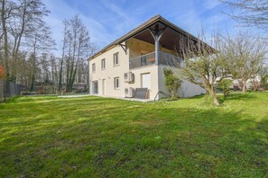 Een gebouw met twee verdiepingen, een balkon, een omheinde tuin en bomen.