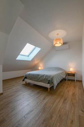 Een slaapkamer met dakraam, een bed, bedlampen en houten vloeren.