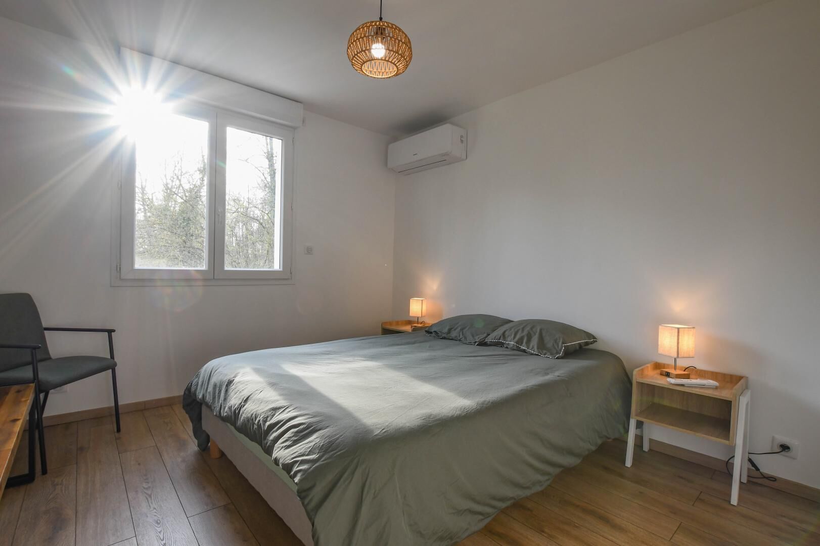 Een slaapkamer met een bed, twee nachtkastjes met lampen, een stoel, een raam en een airconditioning.